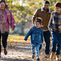一位西班牙裔父亲和一位白人母亲与他们的女儿和儿子在秋天的公园里散步的照片
